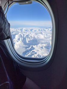Snowy peaks and valleys as seen from an airplane window.