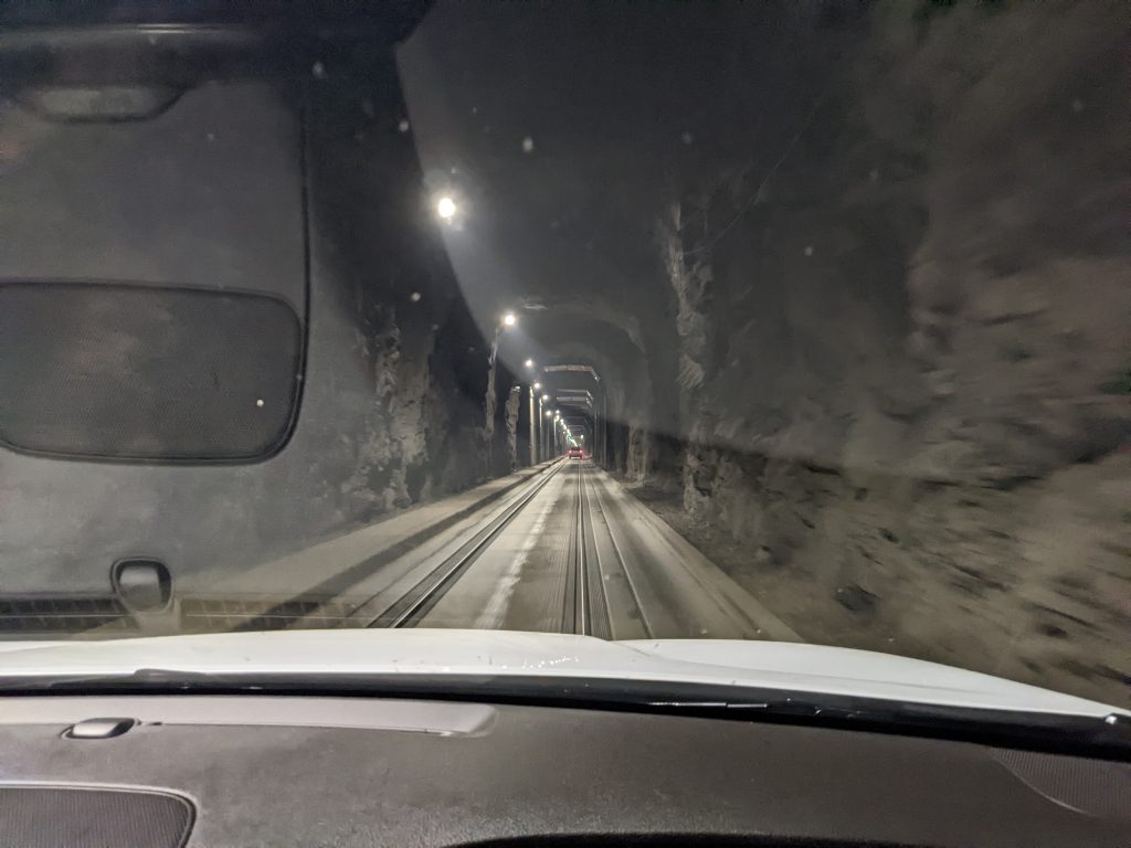 Tunnel with string of lights above and train tracks in the road heading off into the distance.
